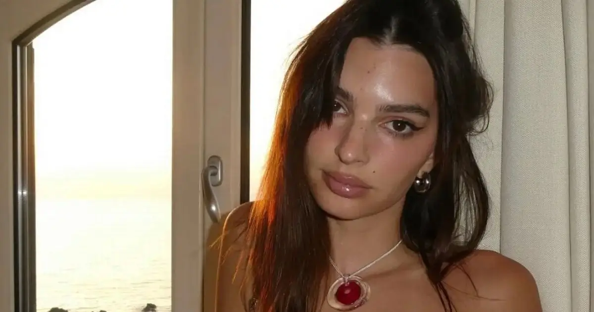 Model Emily Ratajkowski almost bursts out of a black corset top as she leaned against a windowsill