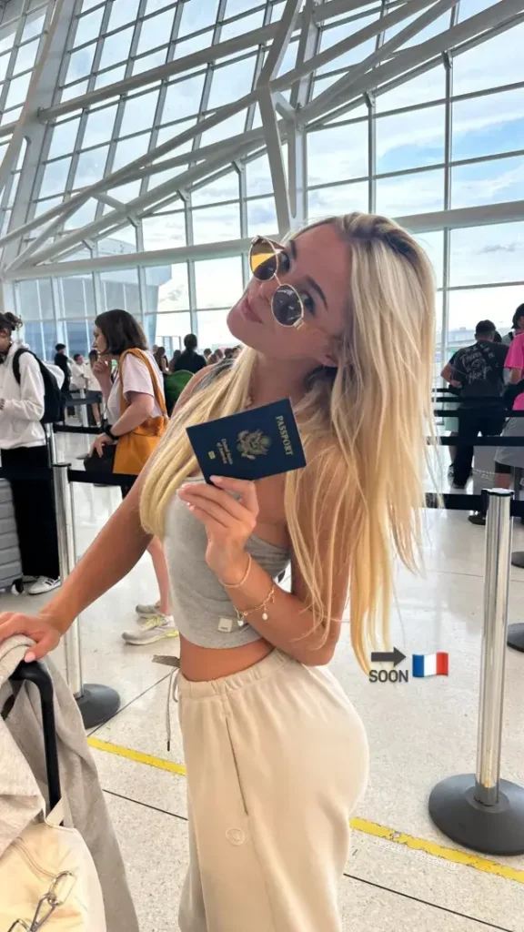 Taking a selfie while holding her passport while wearing cream sweatpants, grey crop tops, and sunglasses, Dunne smiled for the camera. The photo was accompanied by the emojis "soon" and "flag".