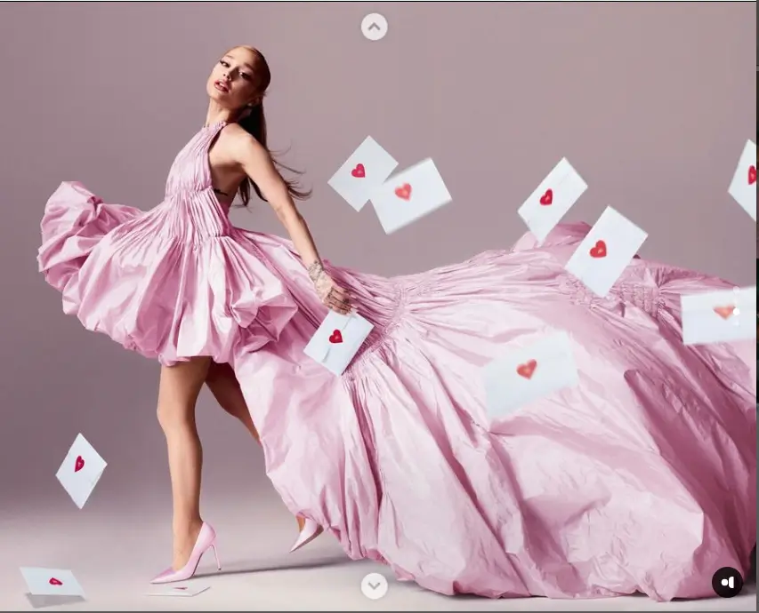 In an announcement video, Grande wore a stunning pink backless gown with a long train and a high hem that showcased her legs in matching heels, surrounded by floating love letters with red heart seals.