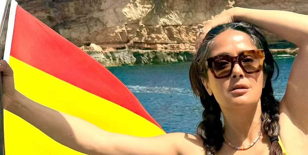 Salma Hayek flaunted her hourglass waistline in a bright yellow low-cut swimsuit as she posed on the boat with the Spanish flag flapping