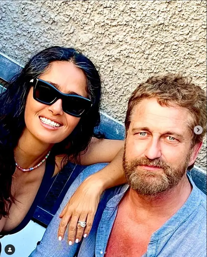 One picture shows Salma smiling while Gerard smolders for the camera in a blue button-up linen shirt. She has large sunglasses on and her raven hair is worn down.