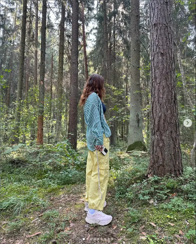 In her opening photo, Bella poses alone amid towering forest trees in yellow cargo pants and a striped shirt . 