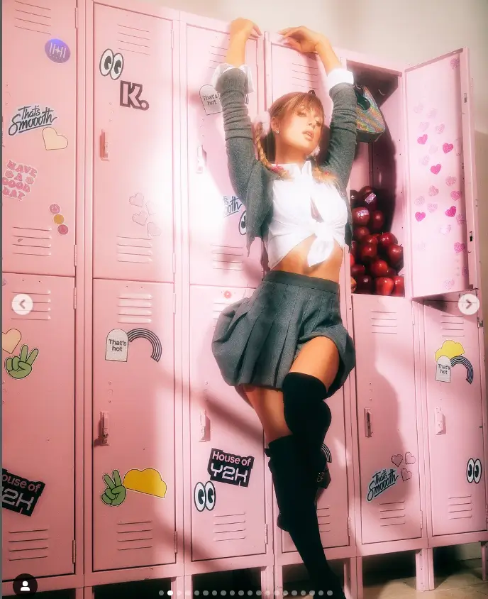 Paris recreated the high school setting from her video by posing with books, a lollipop, and an apple while wearing pleated gray miniskirts and matching wooly cardigans.