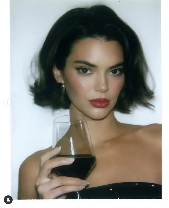 In the second photo, she is seen wearing the same dress while holding a glass of red wine. The stunning ensemble and bold accessory make for a captivating image.