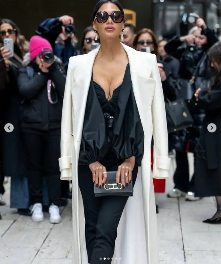 To complete her look, she added a few more inches with sleek black stilettos featuring a white-point. Dressed in a billowing white coat draping over her shoulders, she exuded both comfort and style.