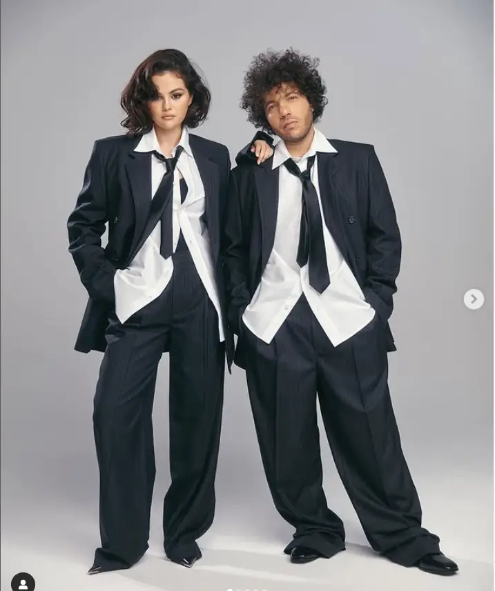 Selena and Benny showed off their impeccable coordinating style in one image, both dressed in matching ensembles of pin-striped dark gray blazers and loose-fitting trousers. To complete the look, they opted for partially buttoned white shirts and black ties, showcasing a sleek and sophisticated fashion sense.