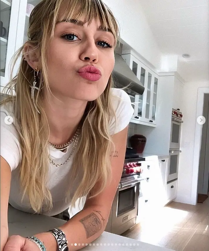 In the gallery, there is a photo of Miley looking effortlessly cool in a white t-shirt and heavy bangs, with one shot capturing her natural beauty outside.