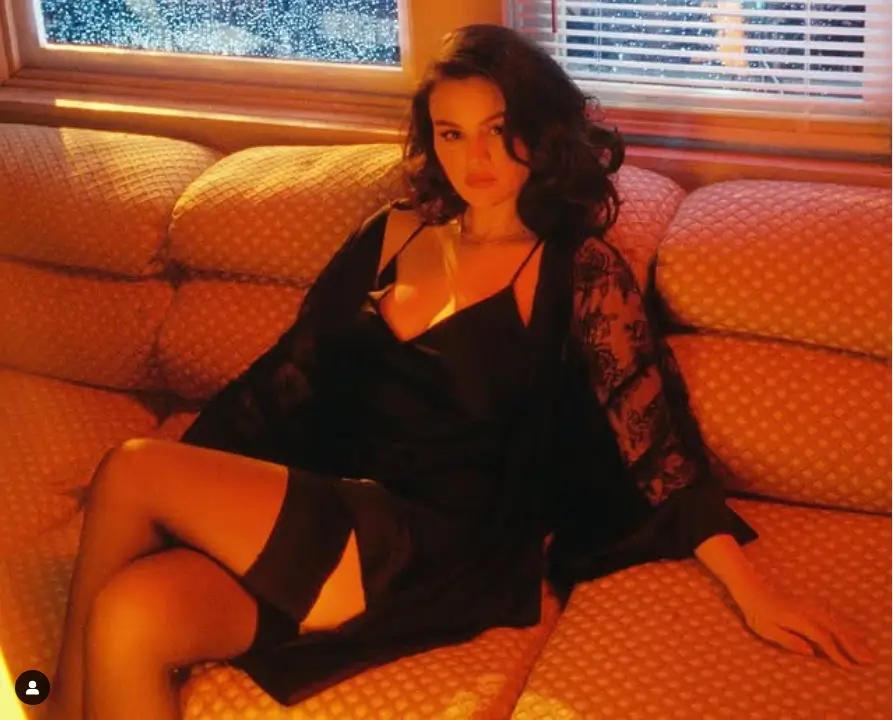 In a seductive outfit of a black negligee, lace robe, and sheer thigh-highs, Gomez exudes sensuality and sets the perfect tone for the romantic track with her sultry pose.